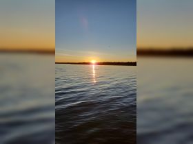 A stunning sunset reflects on the calm waters, creating a picturesque scene perfect for evening boat trips or relaxation by the shore.