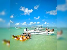 A lively group enjoys a fun day on the water, relaxing on floating mats near a private charter boat in the beautiful turquoise waters of Islamorada.