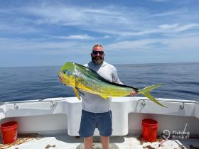 A proud angler displays a vibrant dolphin fish catch aboard a fishing boat, showcasing the thrill of deep-sea fishing adventures.