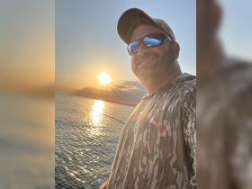 A fisherman captures a selfie against a stunning sunset over the ocean, showcasing the perfect end to a day on the water.