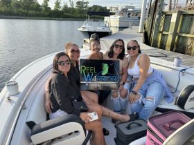 A group of friends enjoys a day out on the water aboard a fishing charter, showcasing their excitement with a sign for 'Reel Warrior Fishing Charters.' Perfect for memorable fishing adventures.