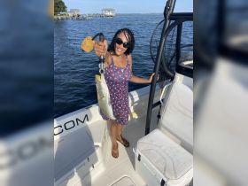 A woman proudly displays her catch while fishing on a boat, showcasing the excitement of a successful day on the water.