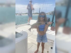 A young girl proudly holds her catch while fishing on a boat, showcasing the joy of family fishing trips in beautiful waters.