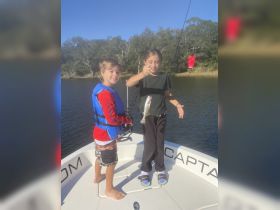 Two children proudly display their catch while fishing on a boat, capturing the joy of a family fishing trip.