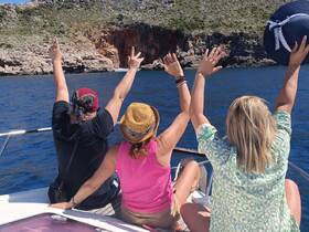 A joyful group of friends celebrates on a boat, raising their hands in excitement against a stunning coastal backdrop — perfect for memorable adventures on the water.