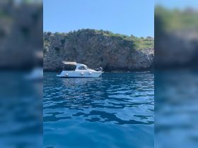 A serene view of a boat anchored near a rocky coastline, showcasing the clear blue waters and natural beauty of the surroundings.