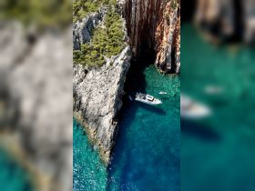 An aerial view captures a boat anchored near a stunning rocky coastline, with people enjoying the clear turquoise waters — a perfect scene for adventure and exploration.