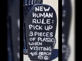A sign at the beach promotes environmental awareness, encouraging visitors to pick up plastic waste to help protect the ocean.