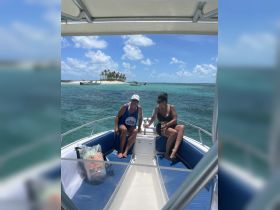 Two friends relax on a boat with a picturesque island backdrop, enjoying a sunny day on the water — perfect for a fun day out with friends.