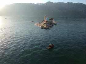 A picturesque view of a serene island with a charming church, as a small boat navigates the tranquil waters during sunset — a perfect scene for exploring coastal beauty.