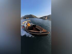 A man navigates a stylish boat through serene waters, surrounded by stunning mountainous scenery — an ideal setting for a memorable boating adventure.