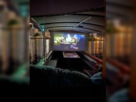 Interior view of a boat featuring a cozy seating area with a movie projected on a screen, perfect for nighttime entertainment on the water.