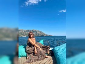 A woman relaxes on the deck of a boat, enjoying the stunning ocean view and mountainous backdrop — a perfect moment for leisure and tranquility on the water.