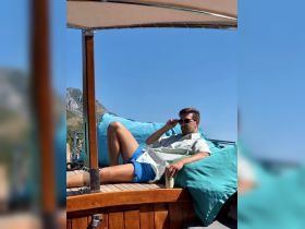 A man relaxes on a boat, enjoying the sun and a drink, perfect for a leisurely day on the water.