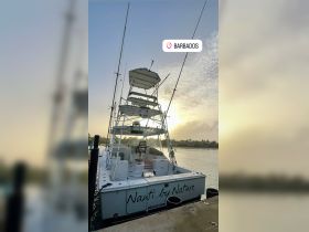 A stunning view of the 'Nauti by Nature' boat docked in Bridgetown, Barbados, with a beautiful sunset backdrop — perfect for fishing adventures or leisure cruises.