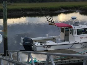 A side view of a fishing boat docked at the marina, showcasing its structure and fishing gear, perfect for a day out on the water.