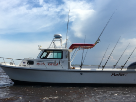 A side view of the fishing boat 'Miss Kayla' anchored in calm waters, showcasing its sturdy design and fishing gear, perfect for a day on the water.