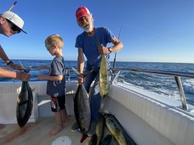 A family enjoys a successful fishing trip, showcasing their catch on a boat in the open ocean — a perfect day for fishing enthusiasts.