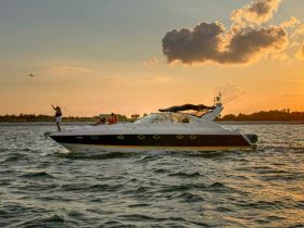 A lively scene of guests enjoying a sunset cruise on a yacht, with one person celebrating at the bow — perfect for memorable outings on the water.
