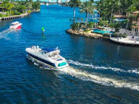 A luxury yacht navigates a scenic waterway, showcasing beautiful waterfront homes and lush palm trees — a perfect setting for a day on the water.