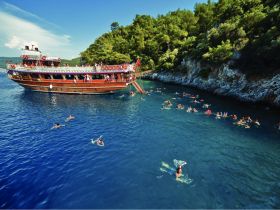 A vibrant scene of swimmers enjoying the clear waters around a wooden boat, perfect for group outings and water activities in a picturesque setting.