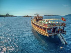 A beautiful wooden boat cruising through sparkling blue waters, showcasing its vibrant deck and inviting atmosphere — perfect for group outings and scenic tours.