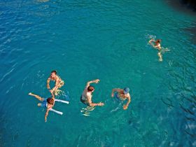 A lively group enjoys swimming in crystal-clear waters, showcasing a fun day of aquatic activities perfect for family outings or group adventures.