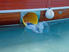 A thrilling moment as a guest slides off the boat into the clear waters, creating a splash — perfect for fun-filled days on the water.