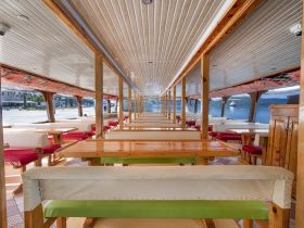 Interior view of a spacious dining area on a boat, featuring wooden tables and comfortable seating, perfect for group gatherings or dining experiences on the water.
