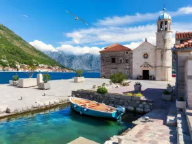 A picturesque view of a small boat docked near charming stone buildings and stunning mountain scenery, perfect for capturing the essence of coastal life.