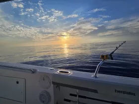 A serene sunset view from the deck of a boat, showcasing calm waters and a fishing rod, perfect for tranquil fishing trips or sunset cruises.