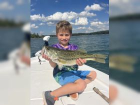 A young boy proudly displays his catch of the day, a large bass, while enjoying a fishing trip on the water — a perfect moment for family fishing adventures.