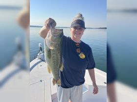 A woman proudly displays her catch of the day, a large bass, while enjoying a fishing trip on the water — a perfect moment for fishing enthusiasts.