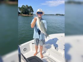 A proud angler holds up a freshly caught striped bass aboard a boat, showcasing the excitement of a summer fishing trip on the water.