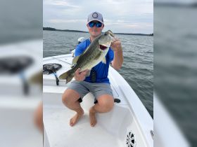 A proud angler displays a large bass caught while fishing from a boat, showcasing the thrill of a successful day on the water.