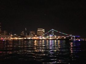 A stunning night view of a vibrant city skyline reflecting on the water, showcasing colorful lights and a lively waterfront atmosphere.