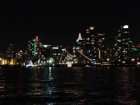 A nighttime view of a city skyline with illuminated buildings reflecting on the water, creating a vibrant urban atmosphere.