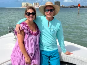 A cheerful couple poses on a boat with a scenic waterfront backdrop, perfect for capturing memorable moments on the water.