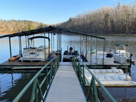 A serene view of a docked pontoon boat at a lakeside marina, surrounded by calm waters and wooded scenery, perfect for relaxing outings.