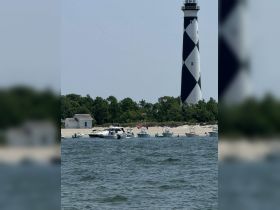 A scenic view featuring a lighthouse with several boats anchored nearby, capturing the essence of a perfect day on the water.