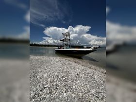 A sleek speedboat rests on a shell-covered beach under a dramatic sky, showcasing the perfect spot for a day on the water.