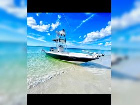 A sleek speedboat rests on the sandy shore under a vibrant blue sky, showcasing the perfect setting for a day on the water.