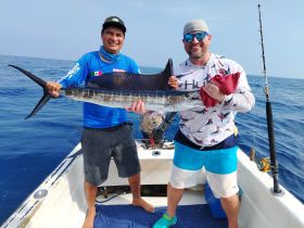 Two anglers proudly display their catch of a marlin while fishing on a boat, capturing the thrill of deep-sea fishing adventures.