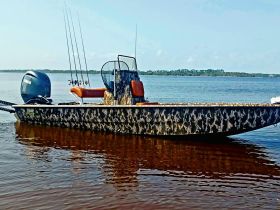 A striking side view of a camouflage fishing boat anchored in calm waters, showcasing its sleek design and fishing gear.