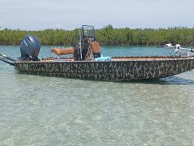 A sleek camouflage boat anchored in shallow waters, showcasing its unique design and perfect for fishing or exploring coastal areas.
