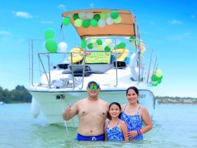 A joyful family celebrates a birthday while wading in shallow waters next to their decorated boat, creating unforgettable memories on the water.
