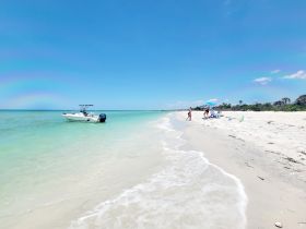 A sunny beach scene featuring a boat anchored nearby while a group enjoys their day on the shore, perfect for a relaxing getaway.
