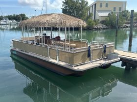 A beautifully designed pontoon boat with a thatched roof, docked in calm waters, perfect for leisurely outings and gatherings.