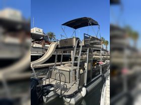A sleek pontoon boat docked at the marina, featuring a slide and spacious seating, perfect for fun-filled days on the water.