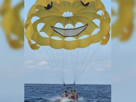 A thrilling parasailing adventure with a group enjoying the stunning views over the water, highlighted by a cheerful smiley face parachute.